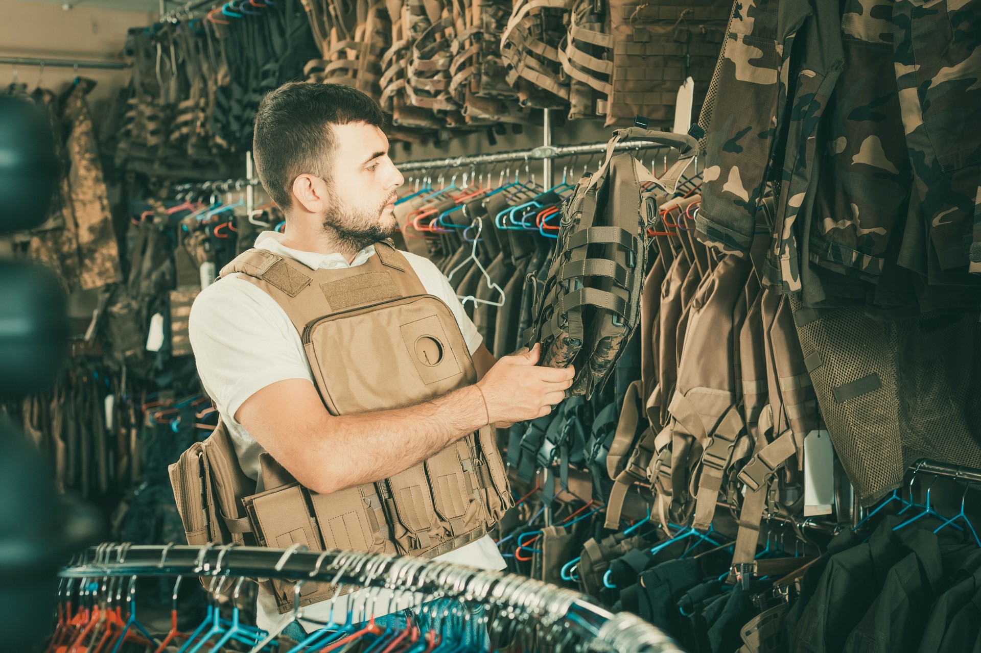Young guy choosing flak jacket in military shop